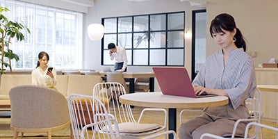 カフェのような雰囲気のオフィスでノートパソコンを開いている女性