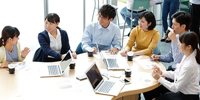 コーヒーを飲みながら会議をする複数人の社員